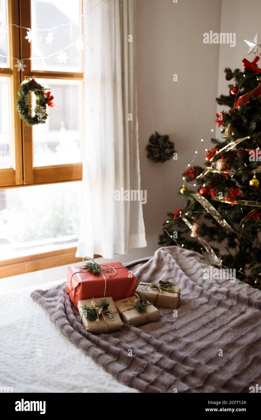 Bett mit Geschenken in rot und Bastelpapier gegen Weihnachtsbaum. Gemütliches Zuhause Weihnachten Urlaub Hintergrund. Stockfoto