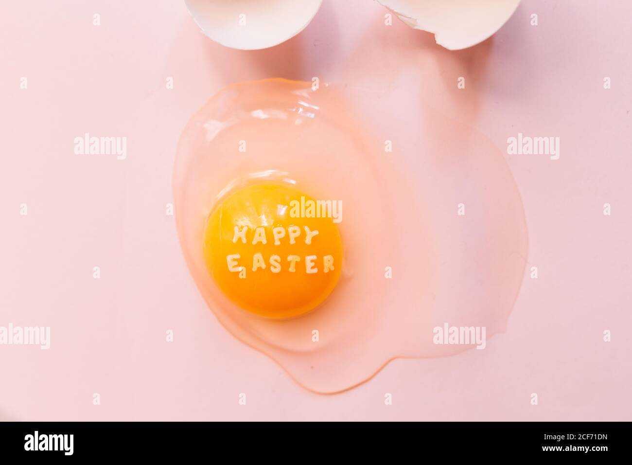 Von oben rohes zerbrochenes Ei mit Text Happy Easter on Gelbes Eigelb und Eierschalen auf rosa Hintergrund Stockfoto