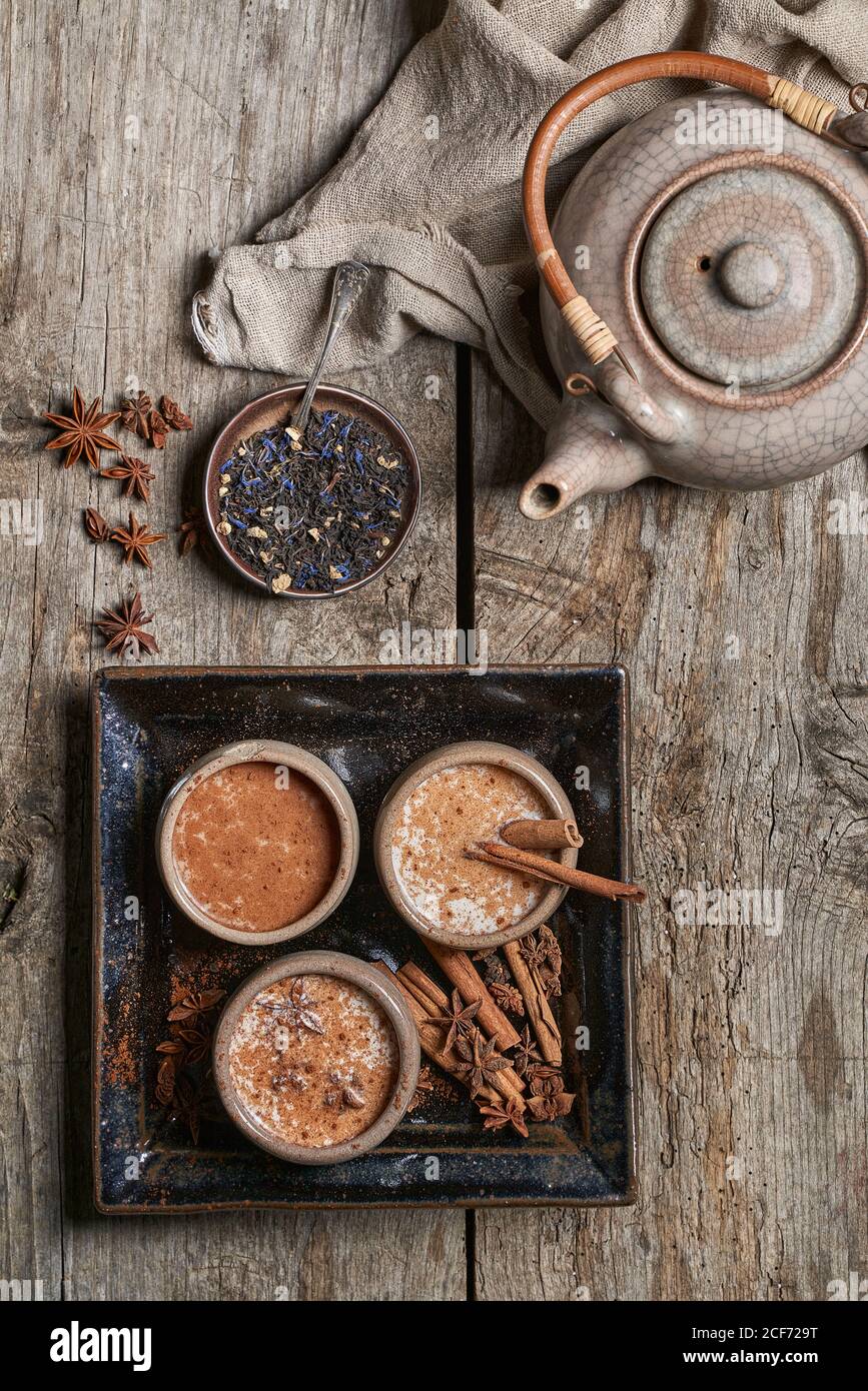 Draufsicht auf Masala Chai serviert in Keramikschalen mit Sternanis und Zimtstangen auf Holztisch mit angeordnet Teekanne und ein Stück Tuch Stockfoto