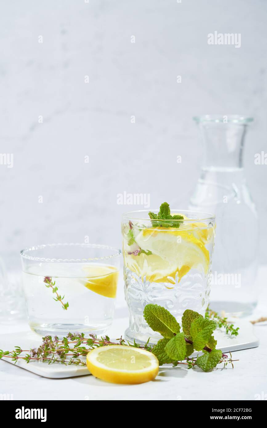 Gläser mit erfrischendem kaltem Thymian und Ingwerlimonade mit Scheiben Von Zitronen- und Minzblättern serviert auf dem Tisch in Licht Zimmer Stockfoto