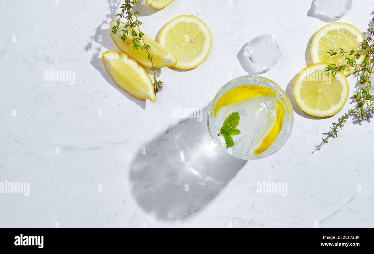 Von oben Gläser mit erfrischendem kaltem Thymian und Ingwerlimonade Mit Scheiben Zitronen- und Minzblätter auf dem Tisch serviert In hellem Raum Stockfoto