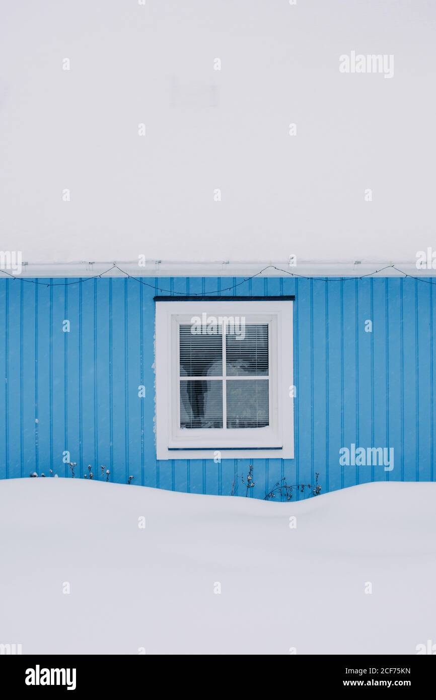 Gebäude mit blauer Wand und Milchfenster zwischen Schneeverwehungen unter Grauer Winterhimmel in der Provinz Schwedisch Lappland Stockfoto