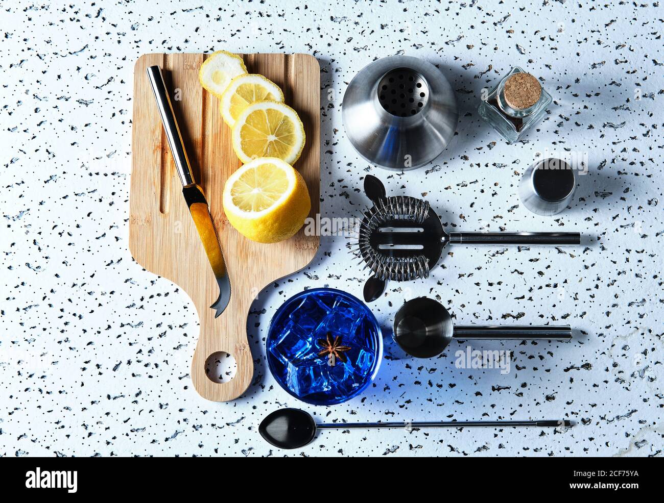 Blick von oben auf blauen Cocktail mit Eiswürfeln und in Scheiben geschnitten Zitrone auf Holzbrett mit Barkeeper-Werkzeug auf Tisch Stockfoto