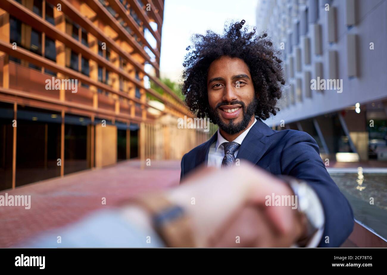 Point of view Aufnahme der lächelnden ethnischen männlichen Unternehmer in Formelle Kleidung schütteln verschwommene Hand von Business Associate und suchen Bei der Kamera Stockfoto