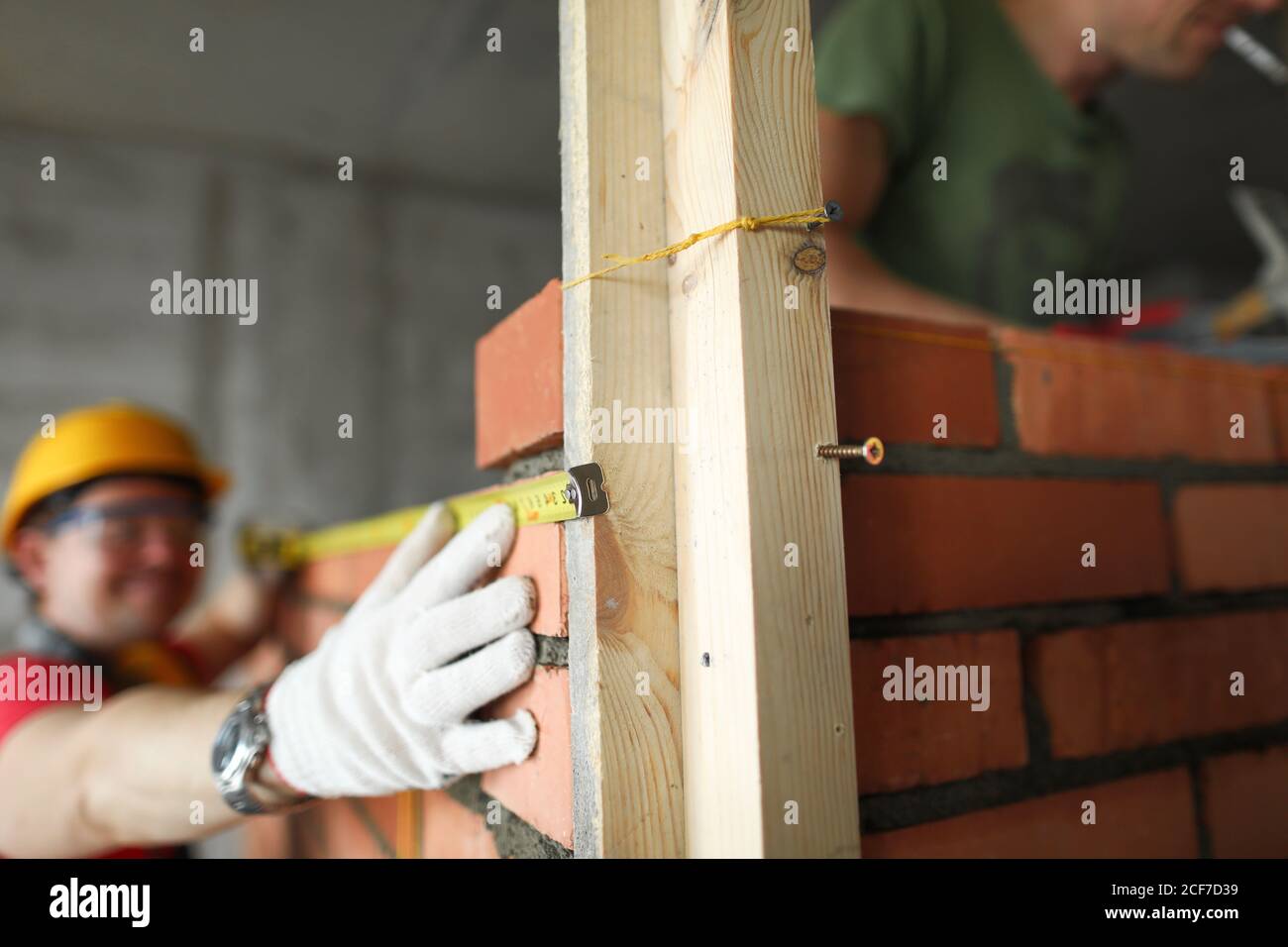 Baumeister nimmt Maßband auf Ziegelwand Nahaufnahme Stockfoto
