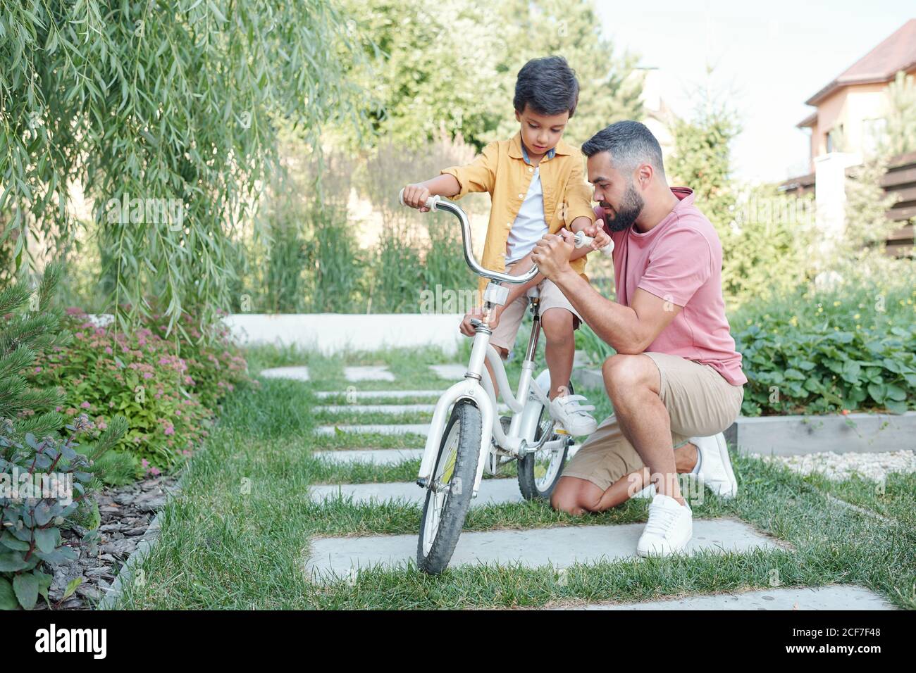 Kleiner Junge, der im Fahrrad sitzt und auf seinen Vater wartet Fixieren Sie die Lenkerhöhe im Freien an sonnigen Sommertagen Stockfoto