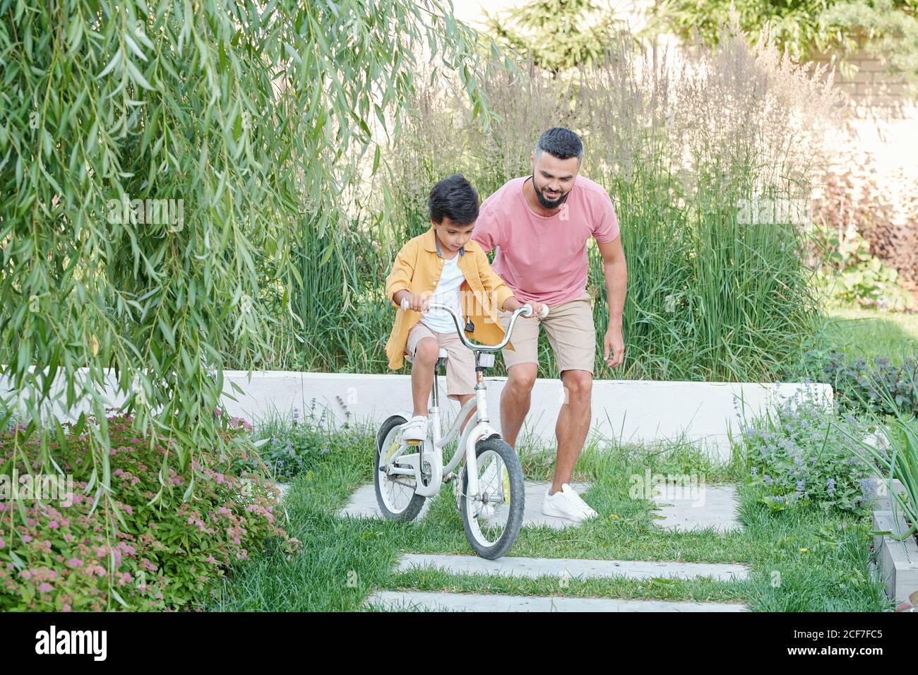 Moderne junge Erwachsene Vater lehrt seinen Sohn Fahrrad im Hinterhof am sonnigen Sommertag fahren, Platz kopieren Stockfoto