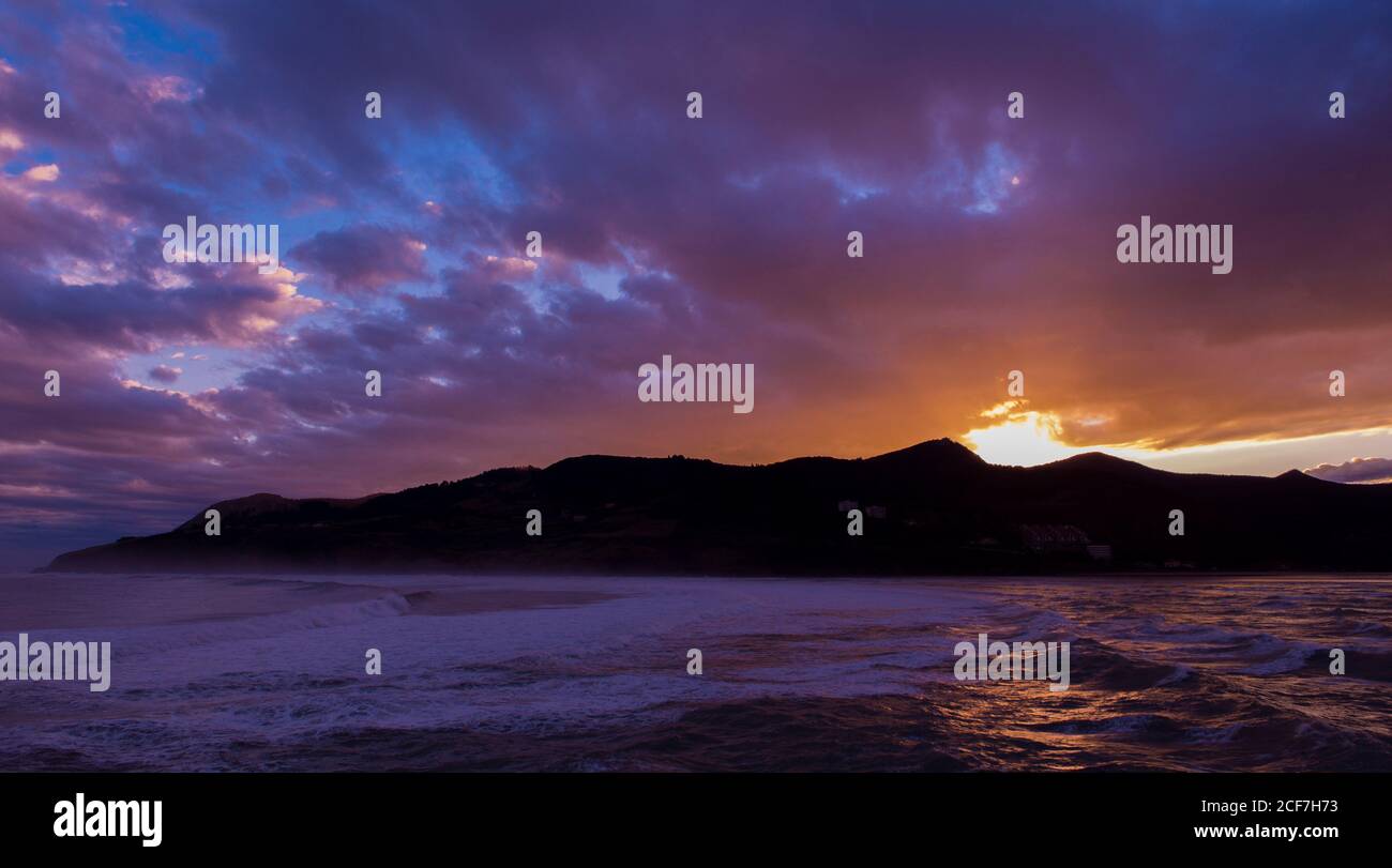 Unglaublicher Sonnenuntergang über bergigen Insel in Oberfläche reflektiert kommen Dunkles Meerwasser Stockfoto