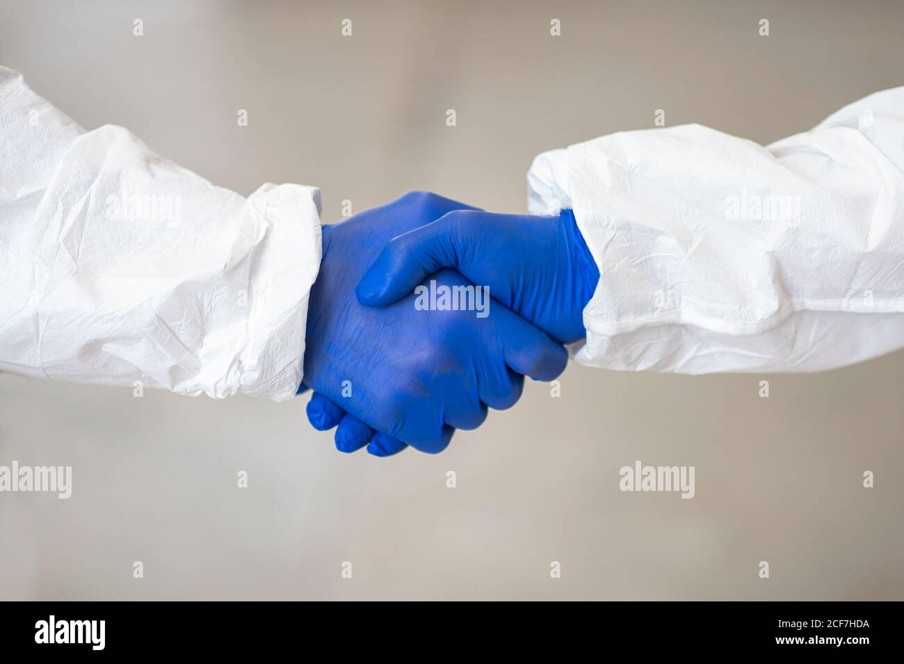 Seitenansicht von nicht erkennbaren Coworking-Praktizierenden in Kostümen und Medizin Handschuhe schütteln Hände während Coronavirus-Epidemie Stockfoto