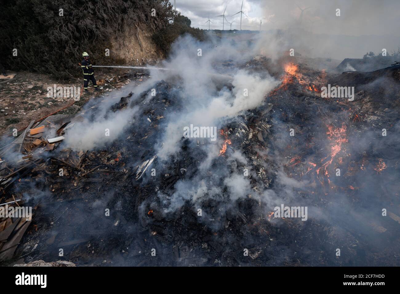 Seitenansicht des tapferen Feuerwehrmans in schützender Uniform stehend mit Schlauch und Löschfeuer auf Müllhalde in Bergen Stockfoto