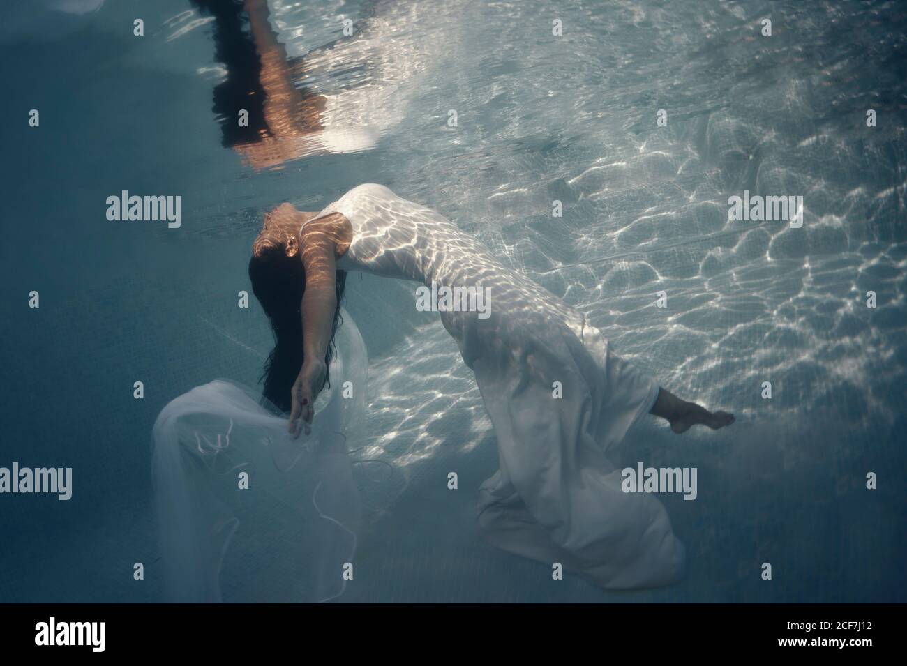 Seitenansicht der schönen langhaarigen Brünette in langen weiß Hochzeitskleid mit Schleier schwimmend unter Wasser mit ausgestreckten Armen Stockfoto