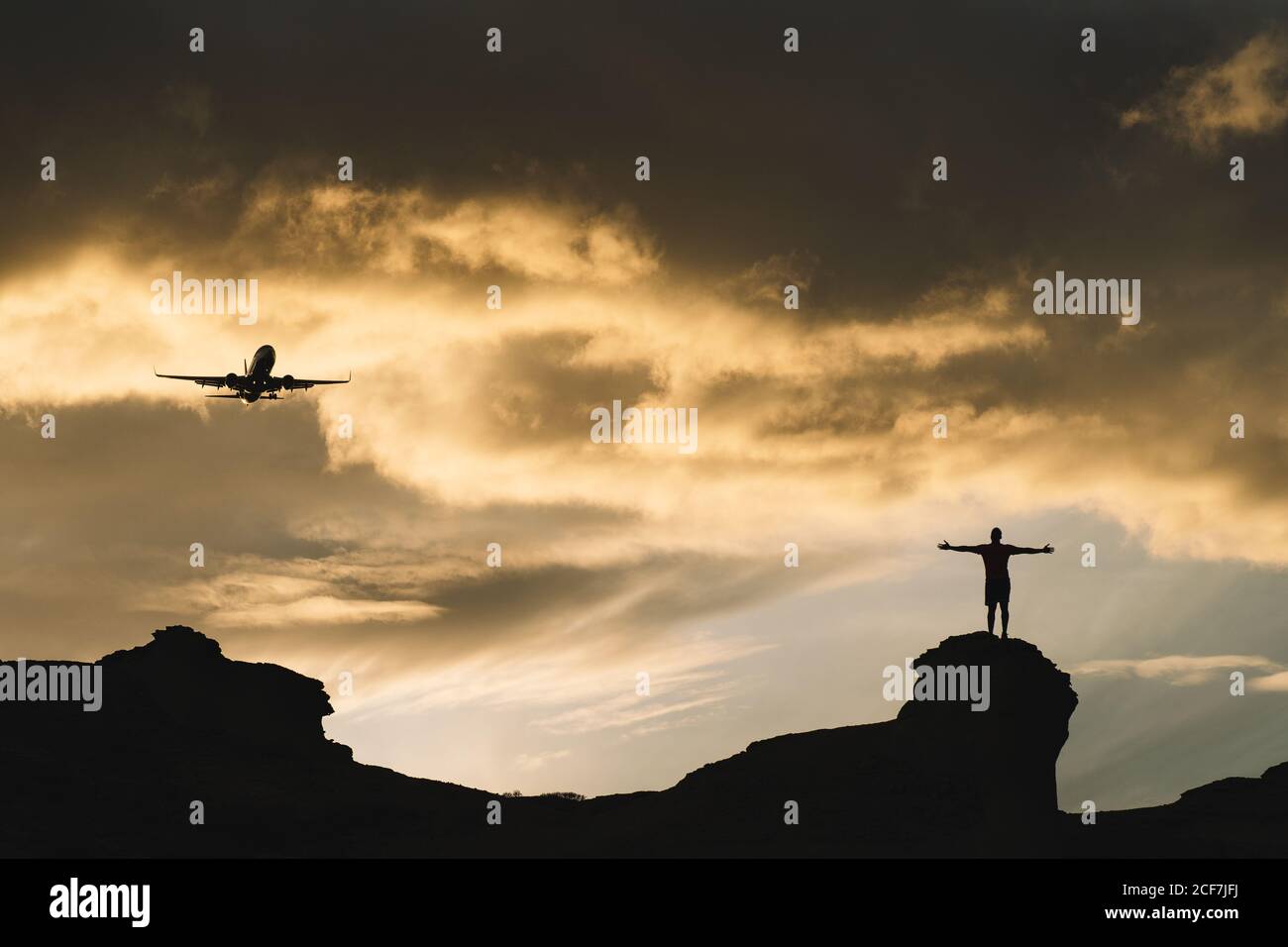 Von unten der menschlichen Silhouette, die auf einem Hügel steht und aufsteigt Hände mit schlichten in schönen bewölkten Himmel auf Sonnenuntergang Stockfoto
