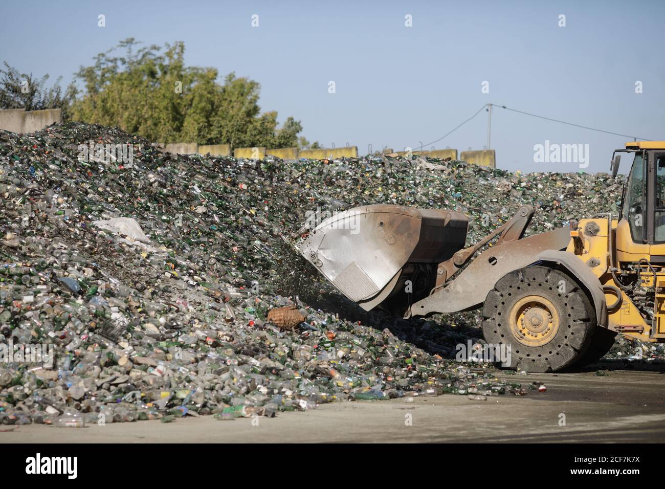 Bucharest, Romania - September 1, 2020: Earth mover operator arranging a pile of empty bottles in a glass recycling facility. Stockfoto