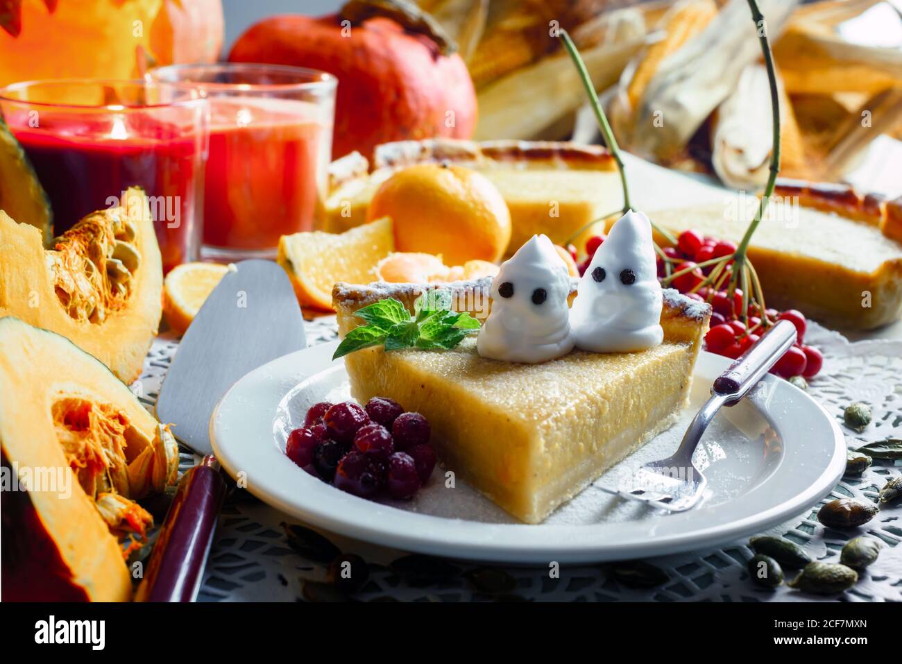 Hausgemachte halloween Kürbiskuchen mit Minzeblatt und kleinen Geistern auf weißem Teller Nahaufnahme. Kerzen und Jack-o-Laterne auf dem Hintergrund. Traditionelles Urlaubsessen Stockfoto