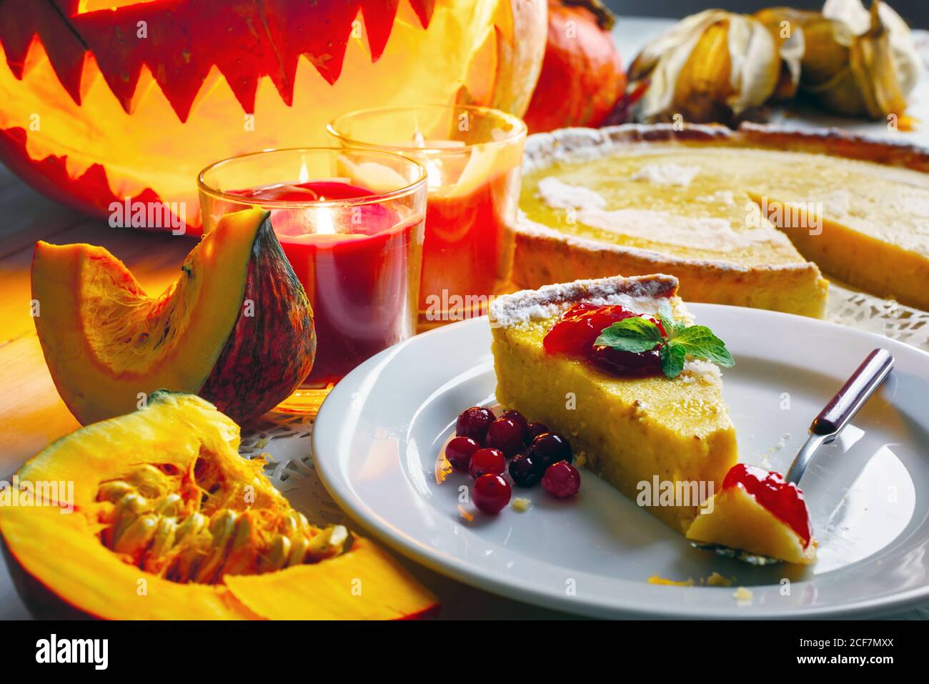 Süße hausgemachte halloween Kürbiskuchen mit Minzeblatt und Preiselbeermarmelade auf weißem Teller Nahaufnahme. Kerzen und Jack-o-Laterne auf dem Hintergrund. Traditionelles Urlaubsessen Stockfoto