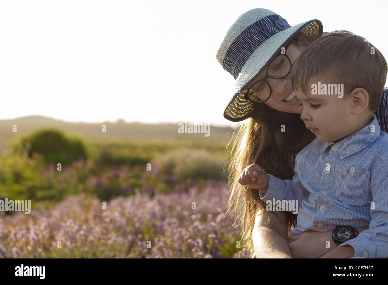 Große Familie, Vaterschaft, Kindheit, Mutterschaft, provence Stil Konzept - glückliche junge Mutter sitzt auf Korbstuhl mit kleinen Jungen Sohn auf Lavendel Stockfoto