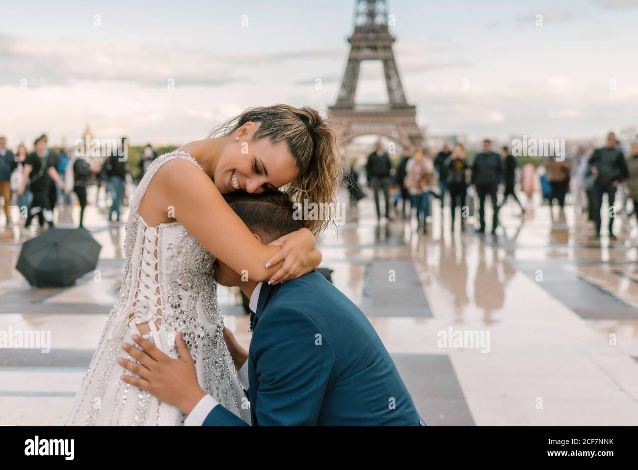 Inhalt Bräutigam in blau stilvoller Anzug auf Knie und Küssen zufriedene Braut in weißem Hochzeitskleid mit Eiffelturm Im Hintergrund Stockfoto