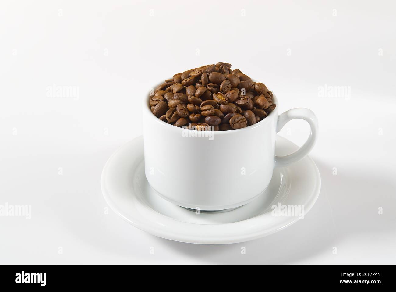 Kaffeebohnen in weißer Tasse, Nahaufnahme. Weiße Kaffeetasse mit Kaffeesamen auf weißem Hintergrund. Konzept für den Internationalen Tag des Kaffees. Stockfoto