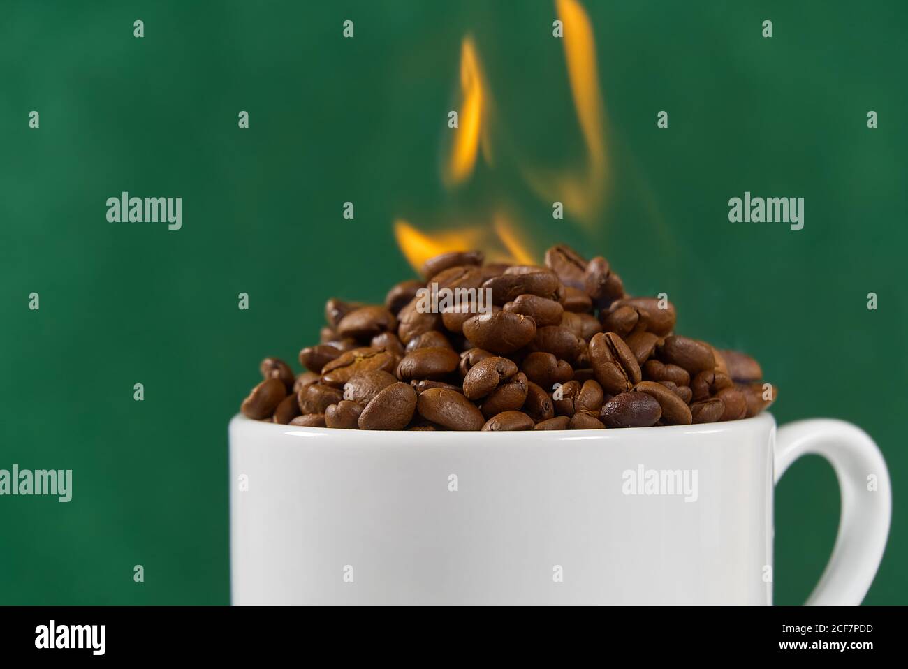 Internationaler Tag des Kaffee-Konzept. Nahaufnahme weiße Kaffeetasse voller Kaffeebohnen auf grünem Hintergrund mit Feuer auf der Oberseite. Stockfoto