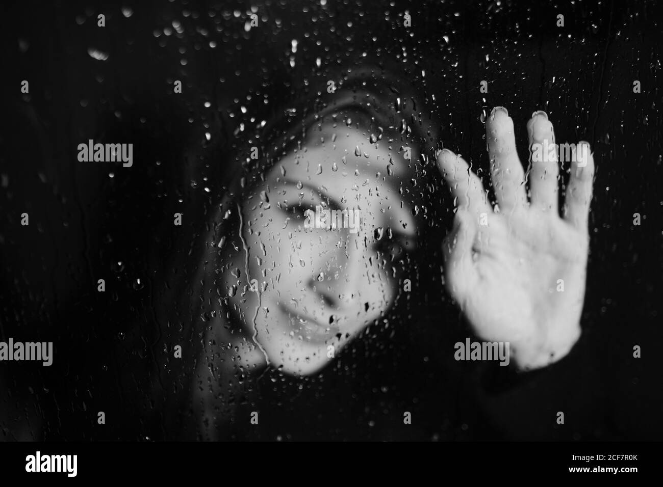 Schwarz und weiß von lächelnder Frau, die hinter Glas im Wasser steht und die Oberfläche berührt und auf die Kamera schaut Stockfoto