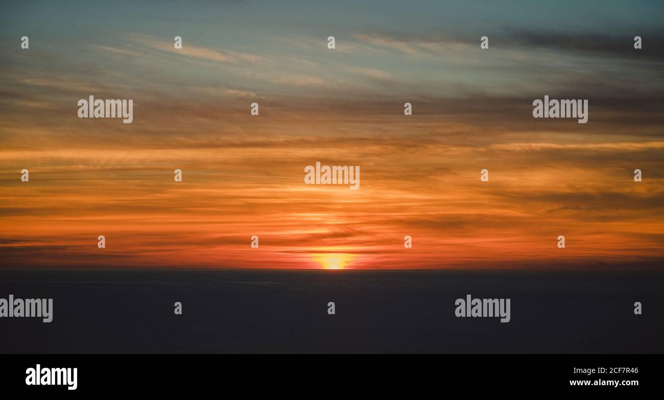 Von oben verschwommener grauer Horizont mit versteckter Sonne unter schönem Bunte Wolken am Himmel mit wunderbarem Übergang in der Dämmerung Stockfoto