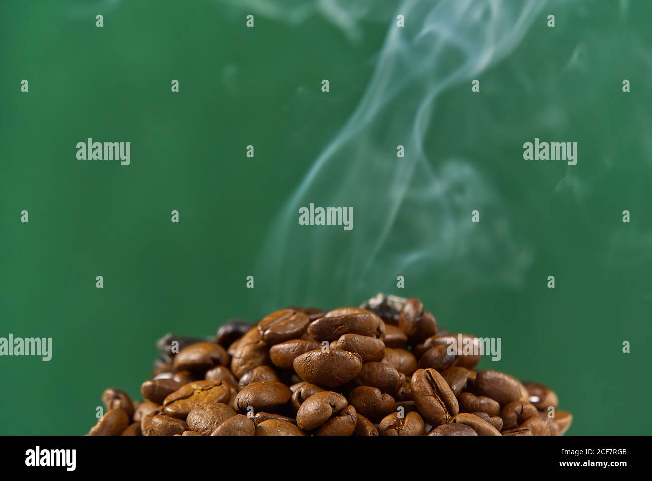 Internationaler Tag des Kaffees Konzept. Nahaufnahme Stapel von Kaffeebohnen auf grünem Hintergrund mit Rauch auf der Oberseite. Stockfoto