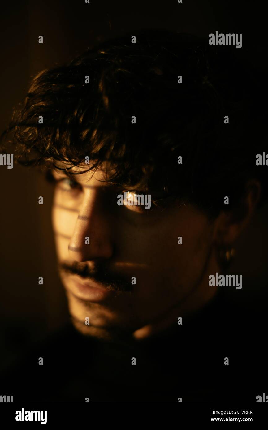 Junger melancholischer Kerl im schwarzen Rollkragen, der neben dem Fenster steht Mit Blenden mit Schatten auf Gesicht Blick auf die Kamera Stockfoto