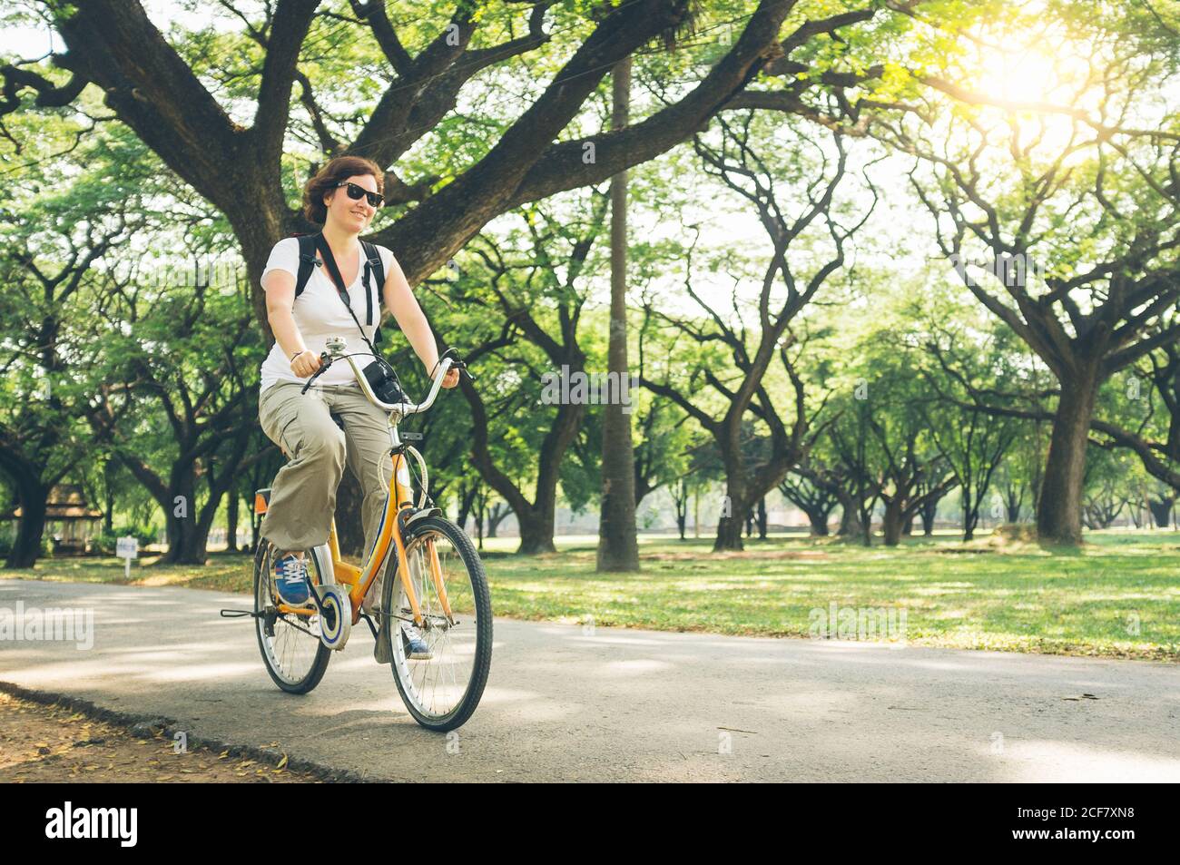 Ziemlich weiblich in casual Outfit Reiten moderne Fahrrad auf dem Weg In der Nähe von grünen Bäumen im schönen Park an sonnigen Tag in Thailand Stockfoto
