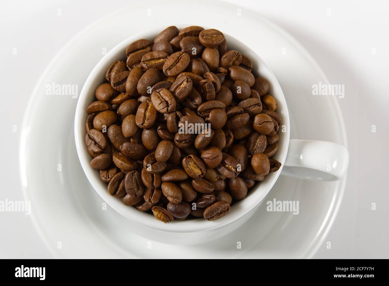 Kaffeebohnen in weißer Tasse, Nahaufnahme. Weiße Kaffeetasse mit Kaffeesamen auf weißem Hintergrund. Konzept für den Internationalen Tag des Kaffees. Stockfoto