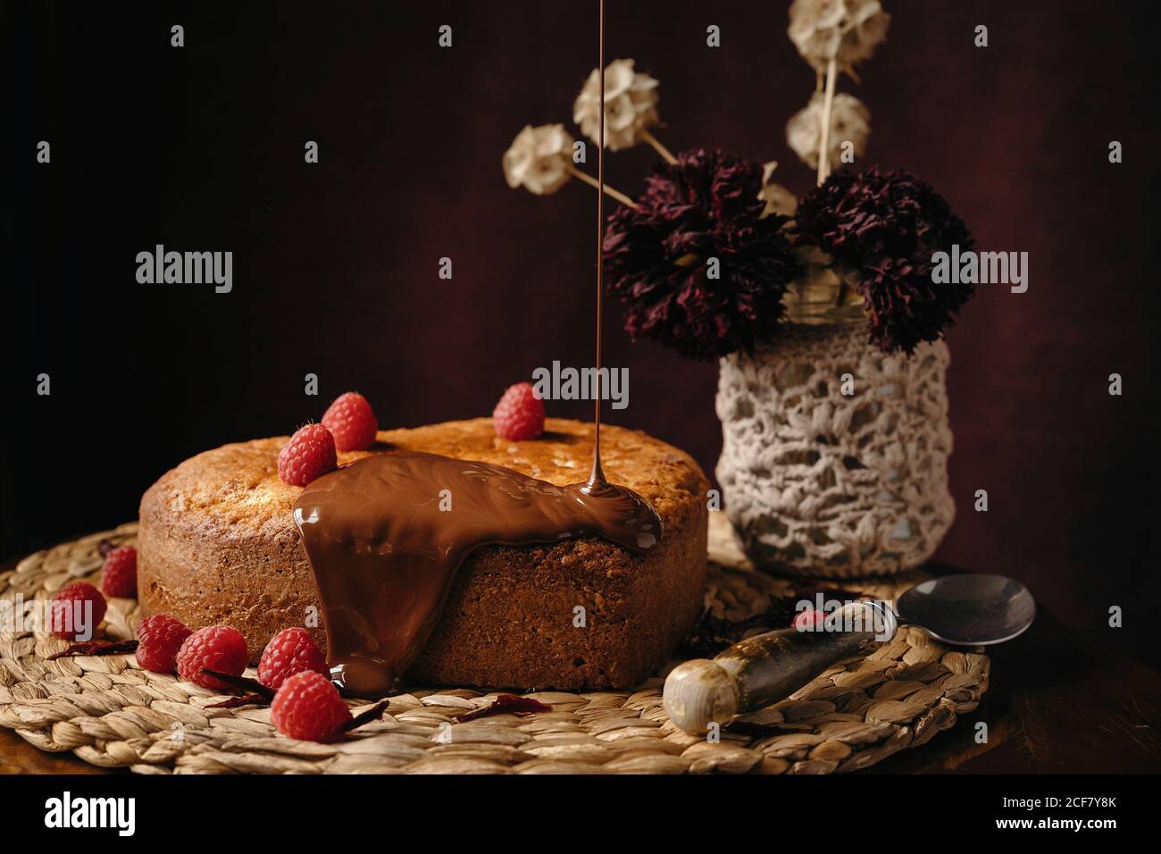 Appetitlich hausgemachter Kuchen mit frischen Beeren, die mit Schokolade gegossen werden Belag auf Korbschale auf Tisch mit Blumen gelegt Stockfoto