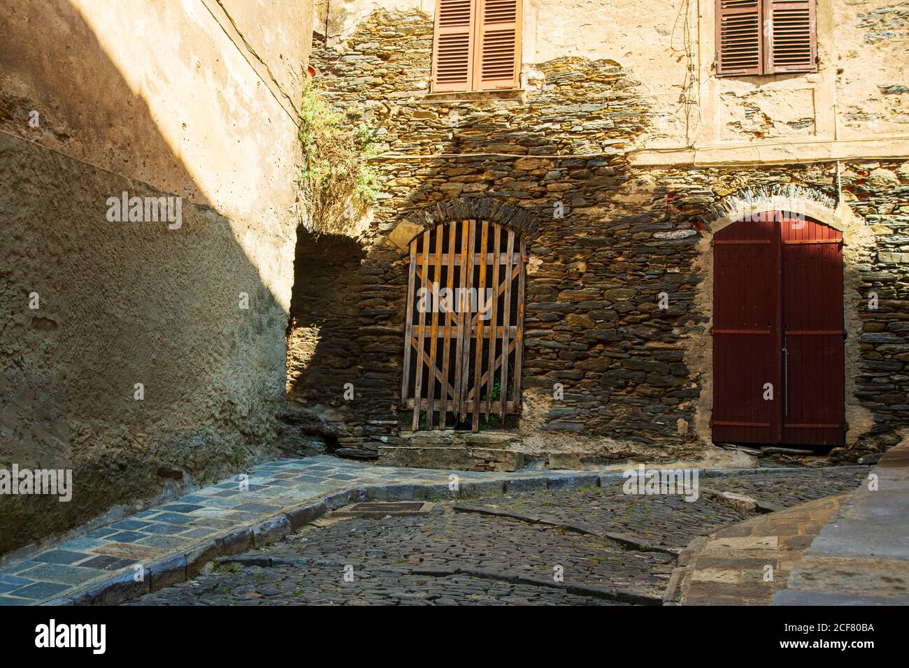 Schmale Gasse mit Kopfsteinpflaster in einem Dorf auf der Insel Korsika in Frankreich im Sommer mit einem schönen Sonnenlicht an den Wänden. Der Eingang des Stockfoto