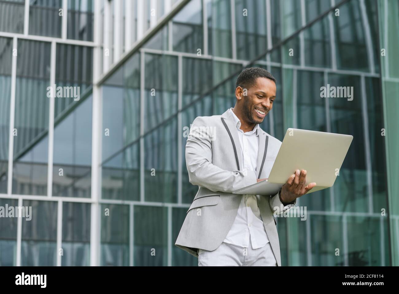Modisch lächelnd afroamerikanischen Geschäftsmann hält Laptop und arbeiten tippen Auf der Tastatur im Hintergrund des Business Centers Stockfoto
