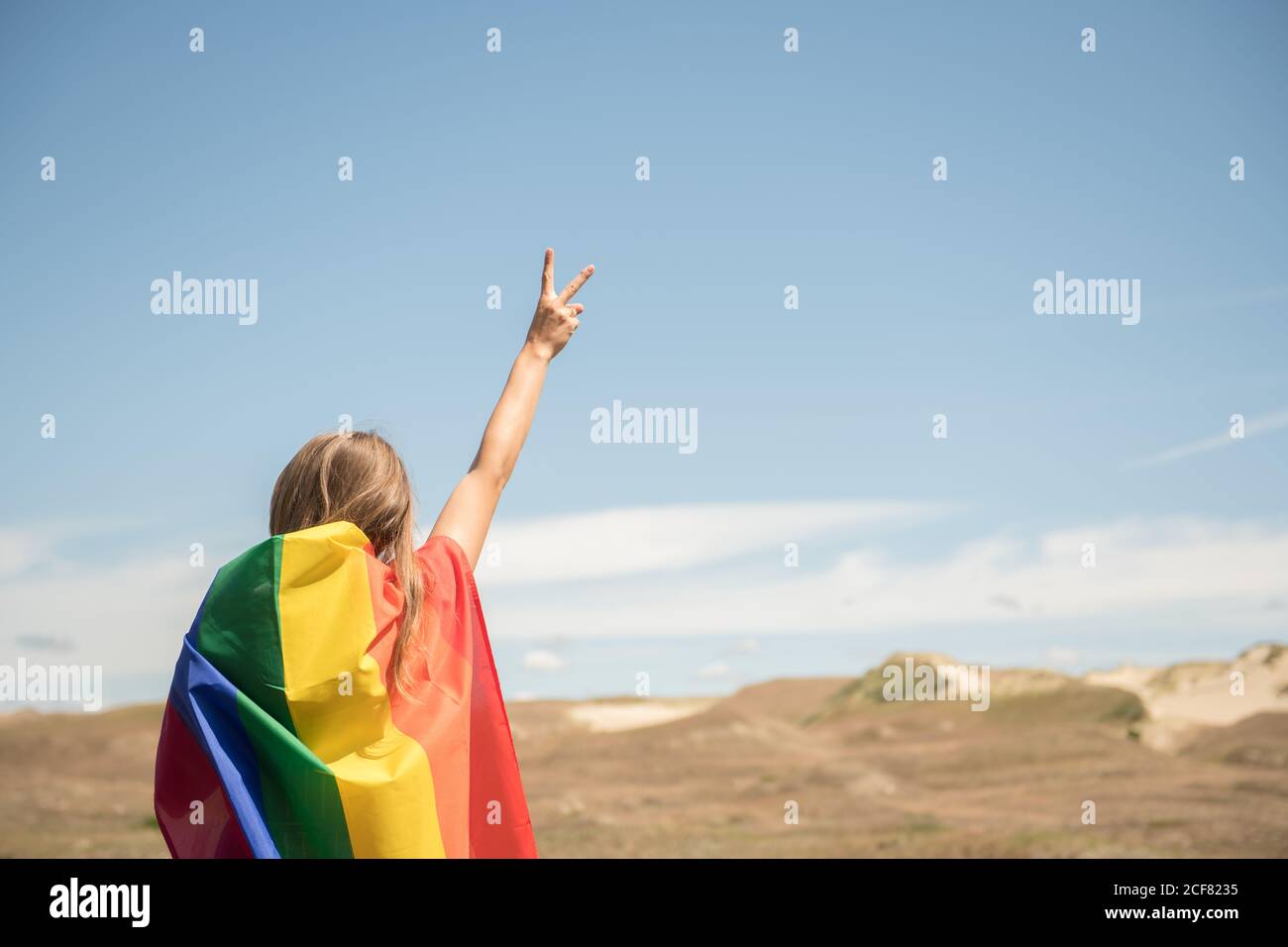 Rückansicht einer selbstbewussten erwachsenen Frau in legerem Kleid, die an windigen Tagen eine Regenbogenflagge über dem Kopf trägt Stockfoto