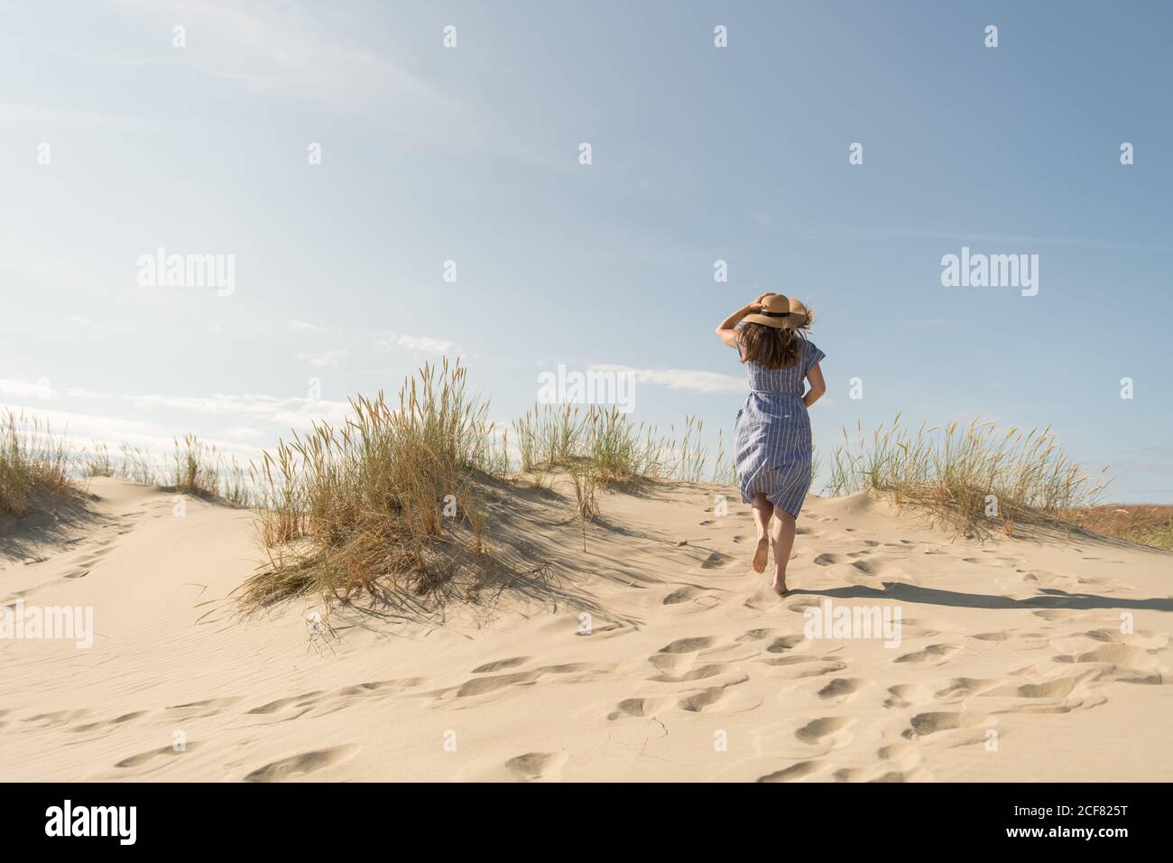 Erwachsene Frau in legerem Kleid und Strohhut beim Spazierengehen mit guter Zeit auf Sanddüne am heißen Sommertag Stockfoto