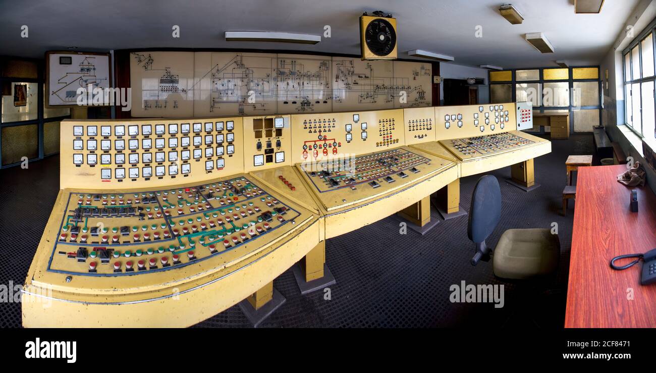Gelbe alte Dashboards mit vielen Tasten Sensoren und Drehrädern in Kontrollraum mit Zeichnungen und Diagrammen an der Wand in menschenleer Bau von Vernachlässigung Kohlebergwerk Stockfoto