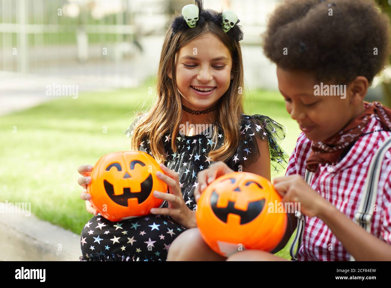 Glückliche Kinder sitzen im Freien und Blick auf Kürbisse Taschen voll Von Süßigkeiten Stockfoto