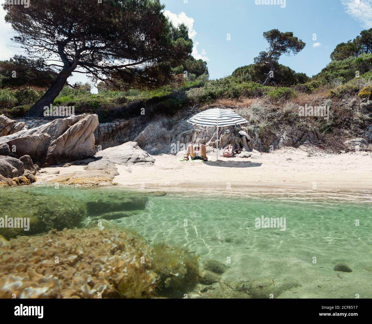 Gebräunter Mann genießen Ruhe unter Sonnenschirm in herrlicher Stelle mit kristallklarem Wasser und Sandstrand im Sommer Tag, Chalkidiki, Griechenland Stockfoto