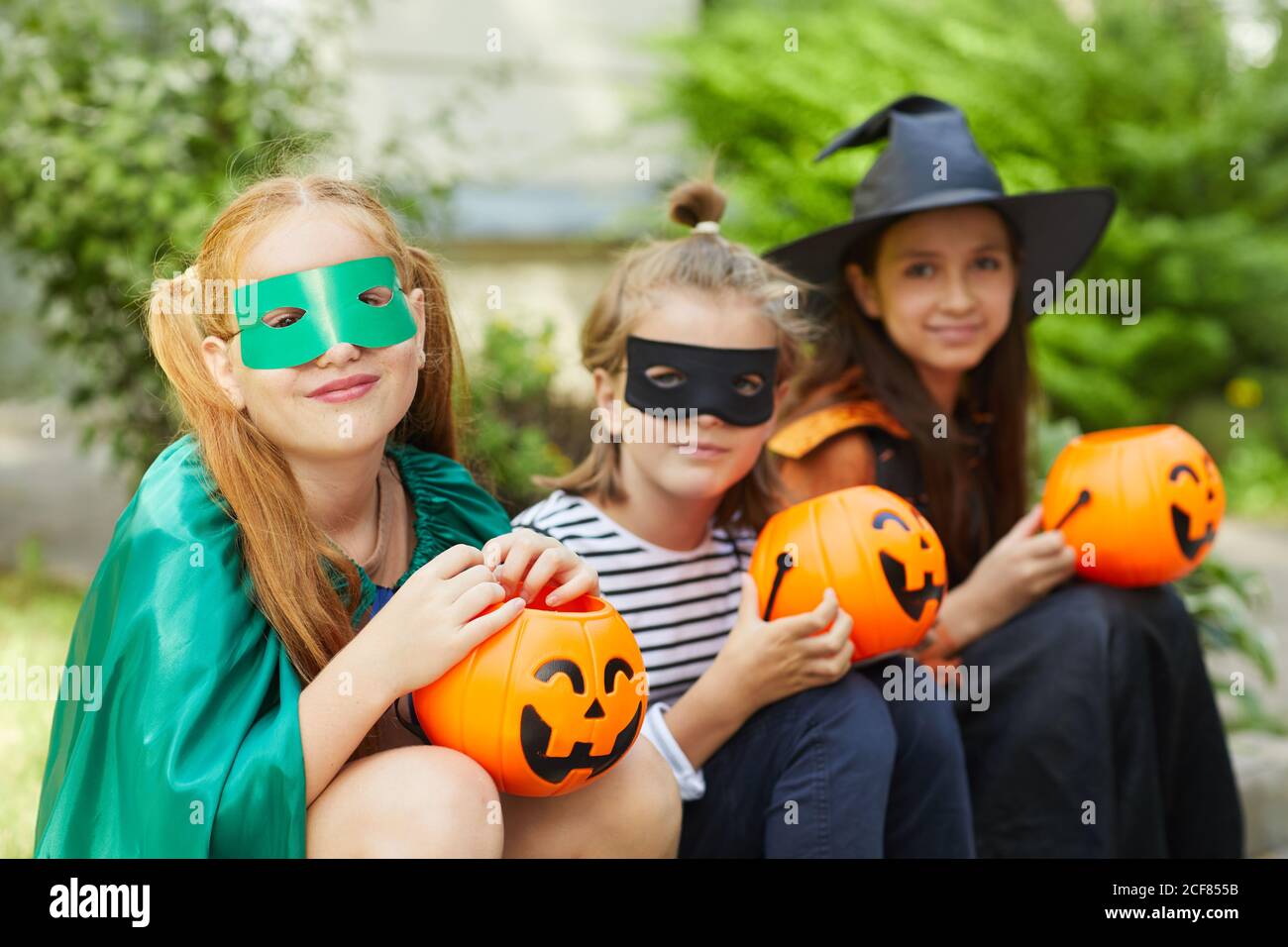 Portrait einer Gruppe von Freunden in Halloween Kostümen mit Spielzeug Kürbisse lächeln bei der Kamera, während sie draußen sitzen Stockfoto