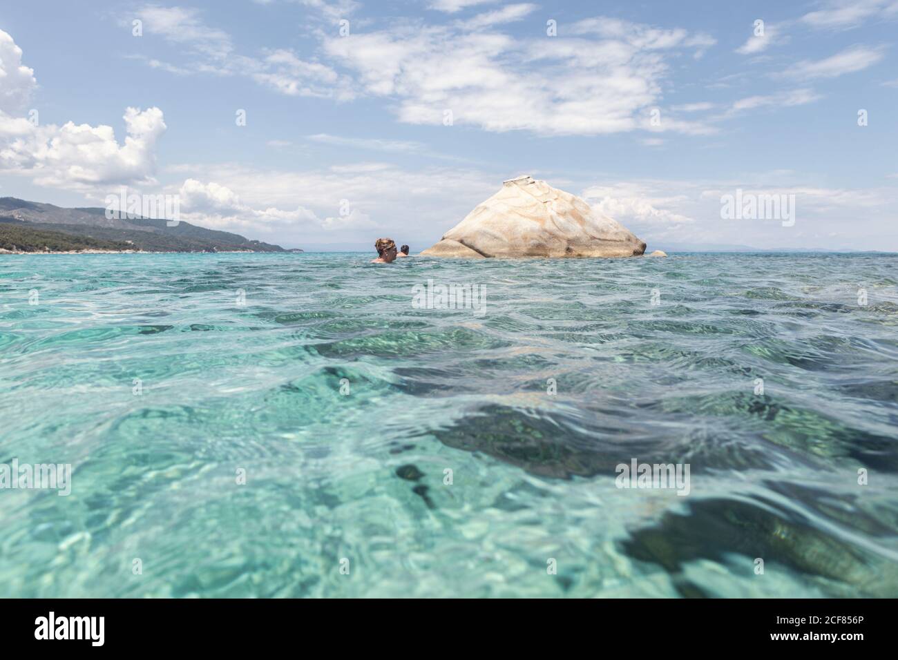 Kristallklares, frisches Wellenwasser mit Schwimmern in der Nähe von großen Felsen am Sommertag in Chalkidiki, Griechenland Stockfoto