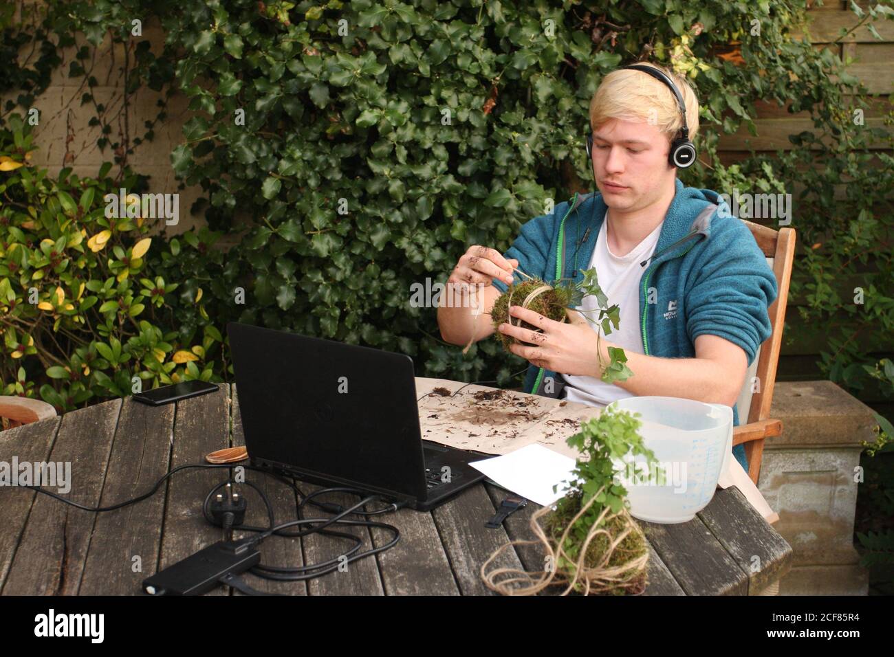 Millennial Generation junger Mann sitzt draußen mit Computer-Anlage Korb zum Aufhängen Stockfoto