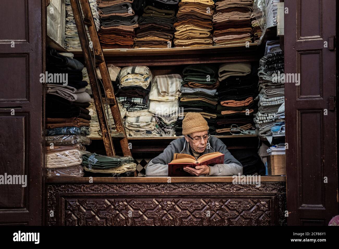 Marrakesch, Marokko - 12. Dezember 2017: Erwachsener Verkäufer Mann sitzt am Schalter mit Stoff und Buch lesen Stockfoto