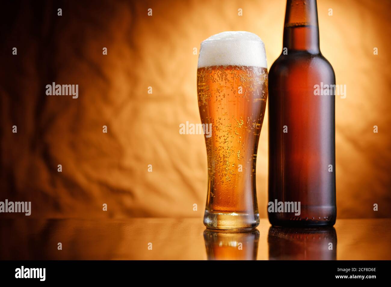 Eisgekühltes Bier in einer unbeschrifteten Flasche und Glas mit schaumigen Kopf und Aufblühen gegen eine rustikale Textur Hintergrund mit Vignette Stockfoto