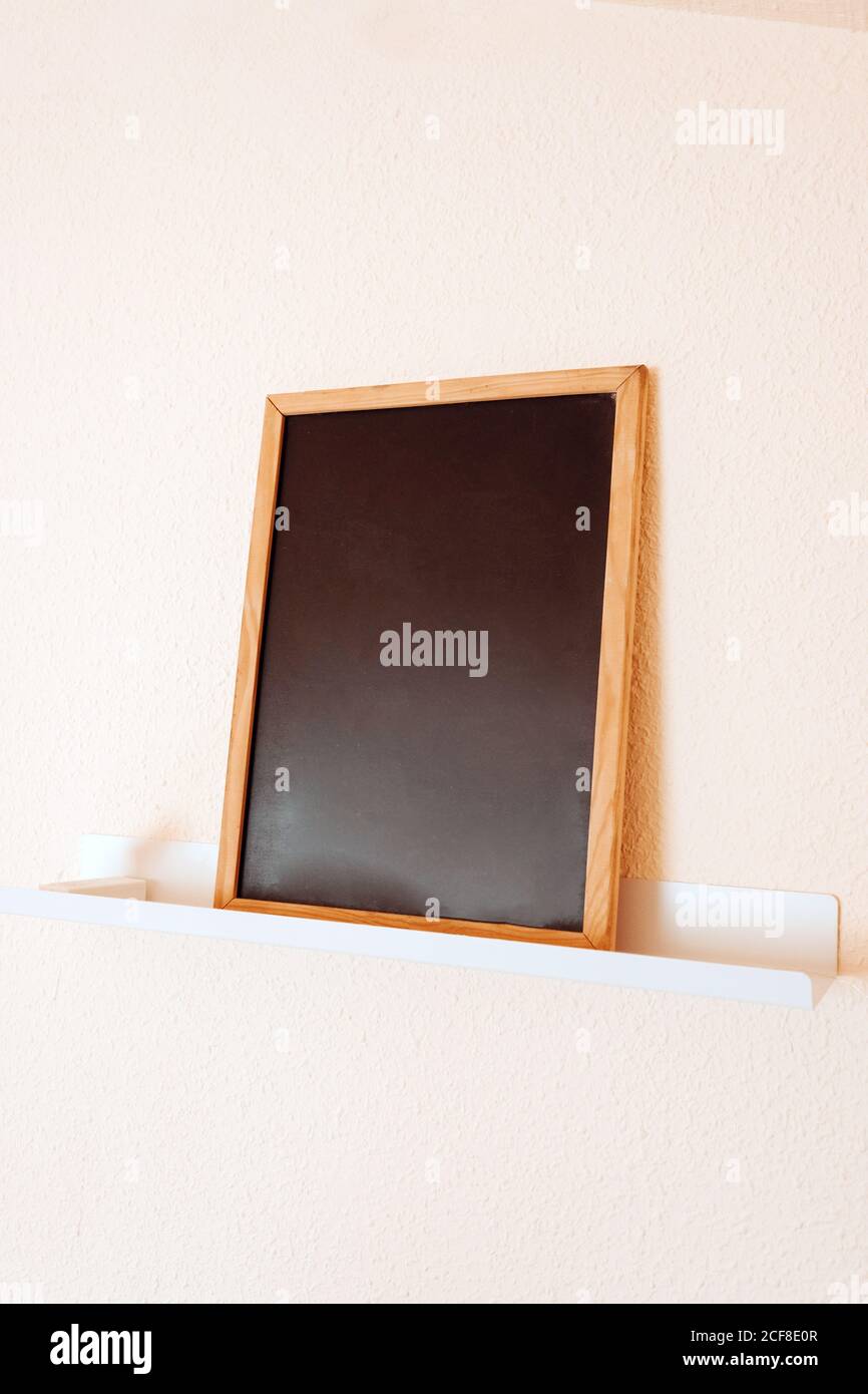 Leere Tafel mit braunem Holzrahmen auf weißem Regal gegen Hellbeigefarbene Wand im modernen Büro Stockfoto
