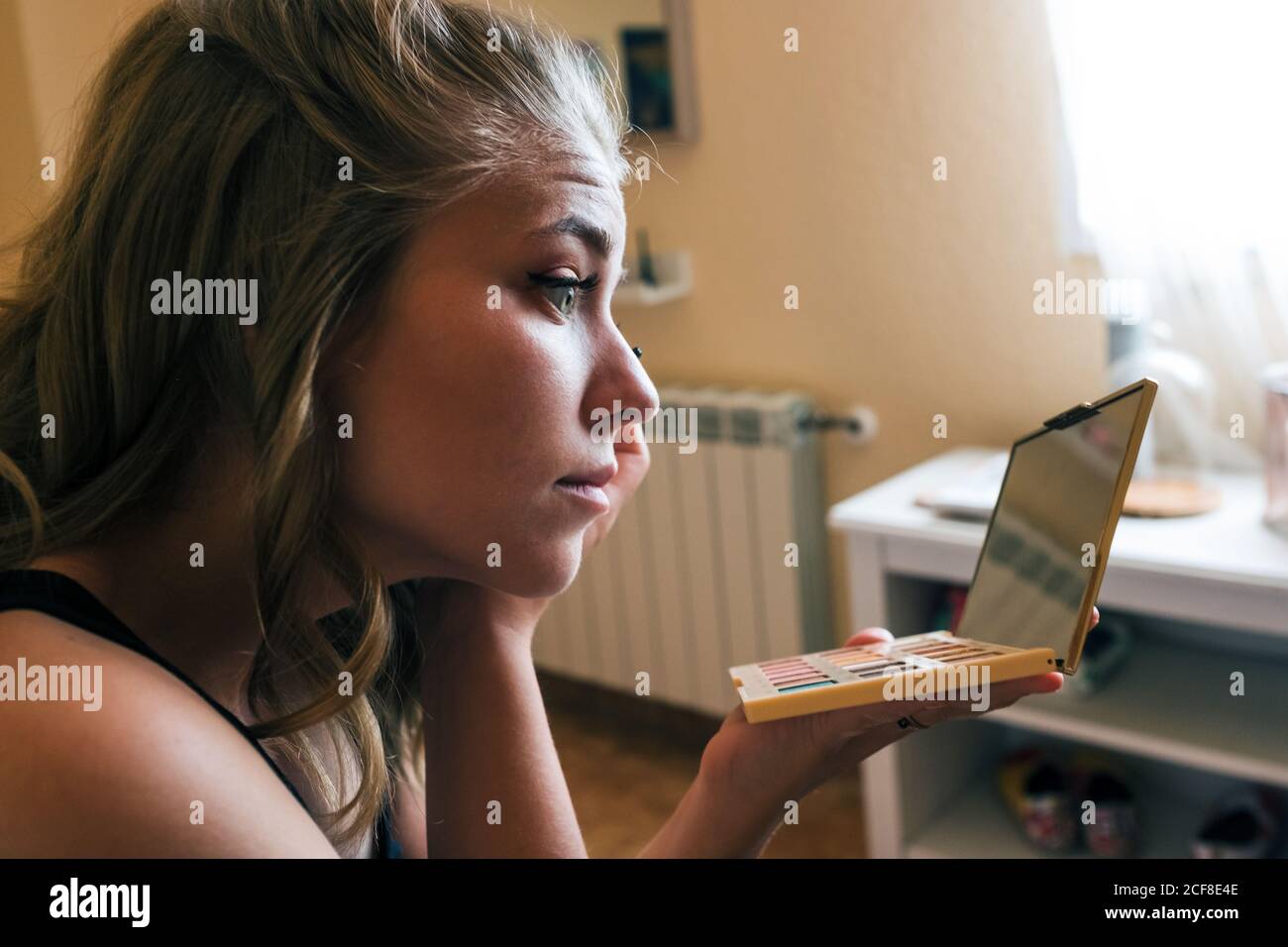 Junge weibliche Holding Palette mit bunten Lidschatten und Spiegel Und Anwendung von schwarzer Mascara auf Wimpern während Beauty-Verfahren bei Zu Hause Stockfoto