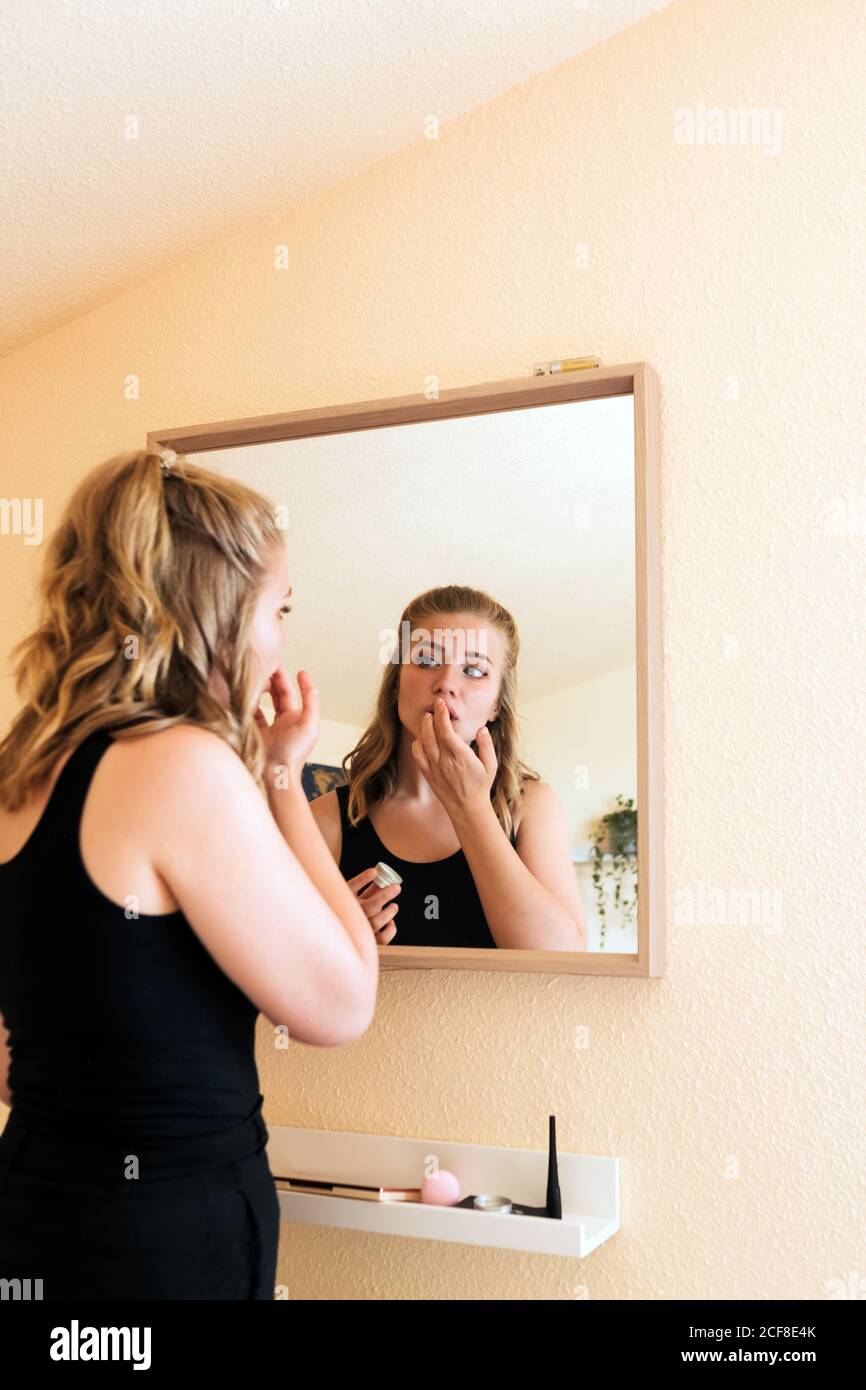 Niedrige Winkel Rückansicht der jungen Frau in lässigem Outfit Haare putzen und Pferdeschwanz machen, während Sie vor stehen Spiegel zu Hause Stockfoto