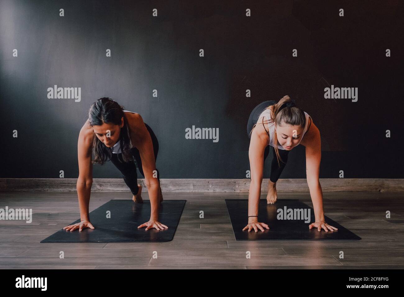 Barfuß Frauen in Sportbekleidung konzentrieren und tun Plank-Übung auf Sportmatten auf Holzboden gegen weiße Wände geräumig Halle Stockfoto