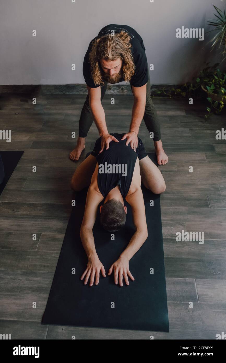 Weibliche Ausbilderin in Sportbekleidung unterrichtet zwei Frauen liegen in balasana Position auf Sportmatten auf Holzboden in geräumigen Training Zimmer Stockfoto