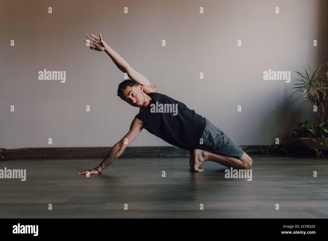 Fleißiger barfüßiger Sportler in Sportbekleidung, der Yoga auf Holzboden praktiziert Im geräumigen, modernen Fitnessraum Stockfoto