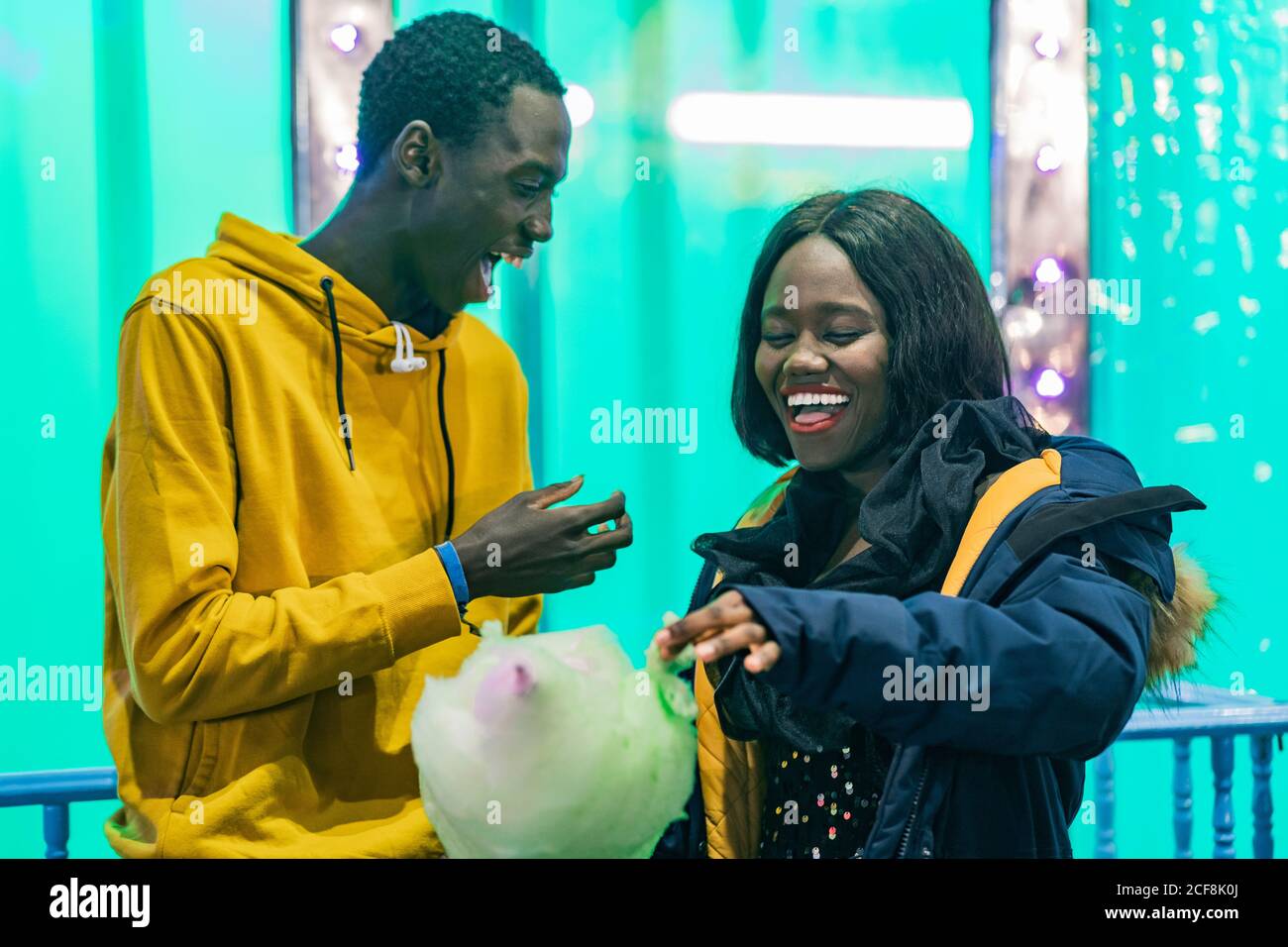 Aufgeregt afroamerikanischen Mann und Frau lachen und essen Zuckerwatte während Datum auf Jahrmarkt Stockfoto
