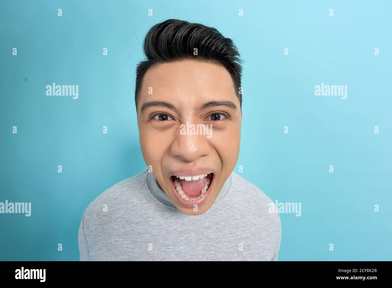 Lautstark auf die Kamera zu sprechen. Ein asiatischer Mann mit grauem T-Shirt und blauem Hintergrund. Stockfoto